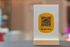 Yellow QR code sign reading 'Scan me' on stand