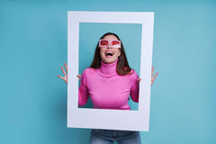 Joyful woman in pink with glasses holding white frame